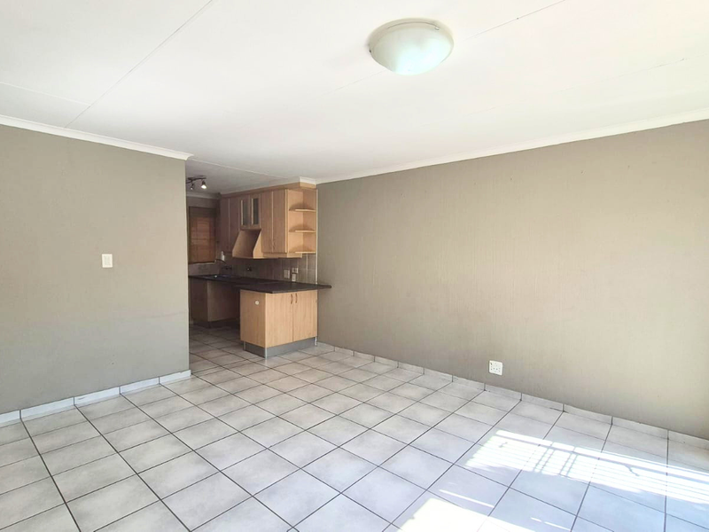 An open-plan living area featuring tiled flooring, neutral walls, and a compact kitchen with built-in cabinetry, leading to a sliding glass door.