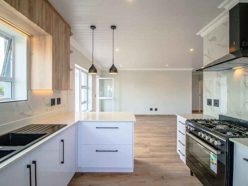 Modern open-plan kitchen featuring sleek white cabinetry, stone countertops, high-end gas appliances, and elegant marble-look splashbacks, flowing into a spacious living area.