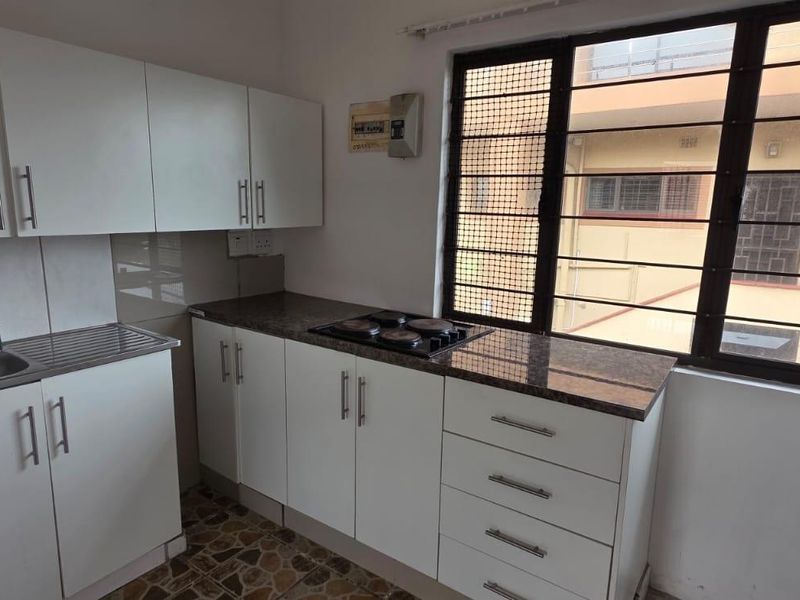 Compact kitchen featuring white built-in cabinetry, granite countertops, an integrated electric hob, and a stainless steel sink with window views.