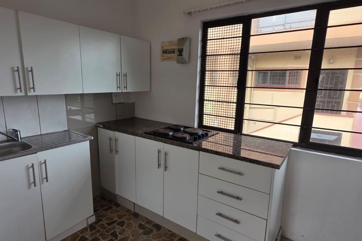 Compact kitchen featuring white built-in cabinetry, granite countertops, an integrated electric hob, and a stainless steel sink with window views.