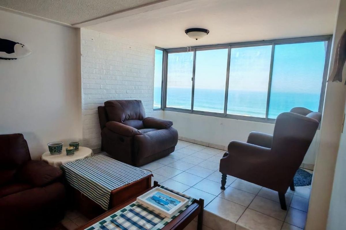 A sunlit living area featuring tiled flooring, a raised platform, and expansive windows offering panoramic ocean views.