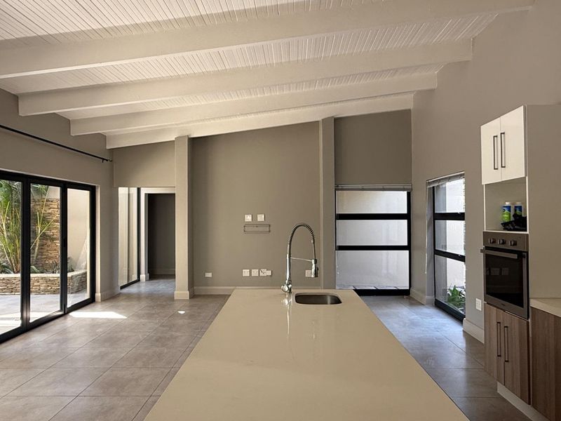 Spacious open-plan kitchen and living area featuring a central island, modern cabinetry, tiled floors, and high exposed beam ceilings with access to a private courtyard.