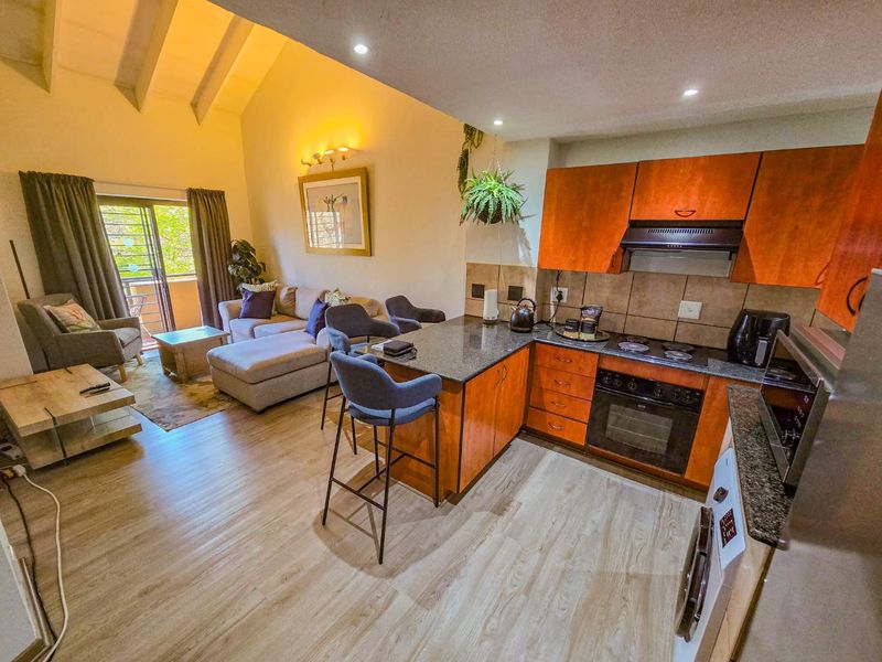 Open-plan living area featuring a kitchen with granite countertops, built-in appliances, and a spacious lounge area with vaulted ceilings and access to a balcony.