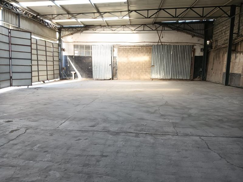 Spacious industrial warehouse unit featuring high ceilings with exposed metal trusses, concrete flooring, and large sliding metal access doors.