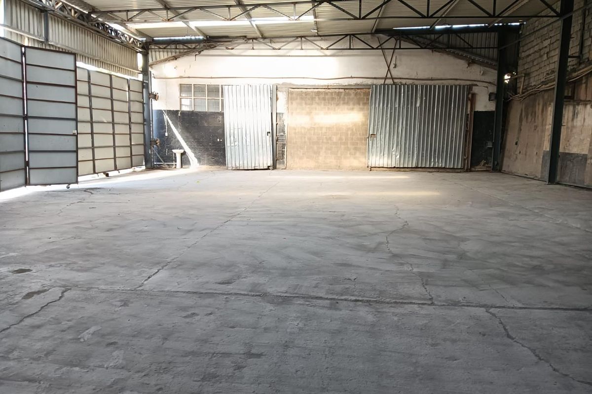 Spacious industrial warehouse unit featuring high ceilings with exposed metal trusses, concrete flooring, and large sliding metal access doors.