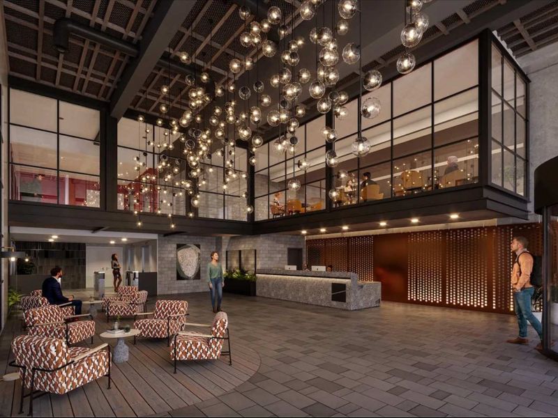 Modern industrial-style lobby featuring a stone reception desk, mezzanine level with glass partitioning, and dramatic decorative pendant lighting.