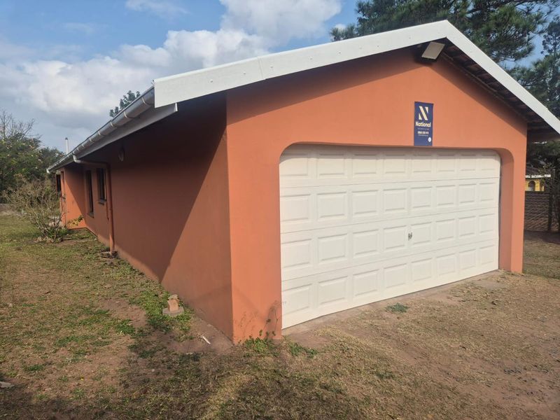 A detached garage building featuring a white sectional door, terracotta-colored exterior walls, and a gable roof structure.