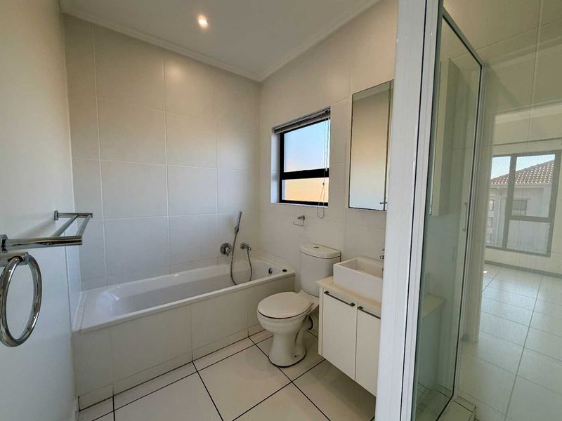 A clean, modern bathroom featuring a bathtub, separate shower enclosure, vanity with basin, and neutral wall and floor tiling.