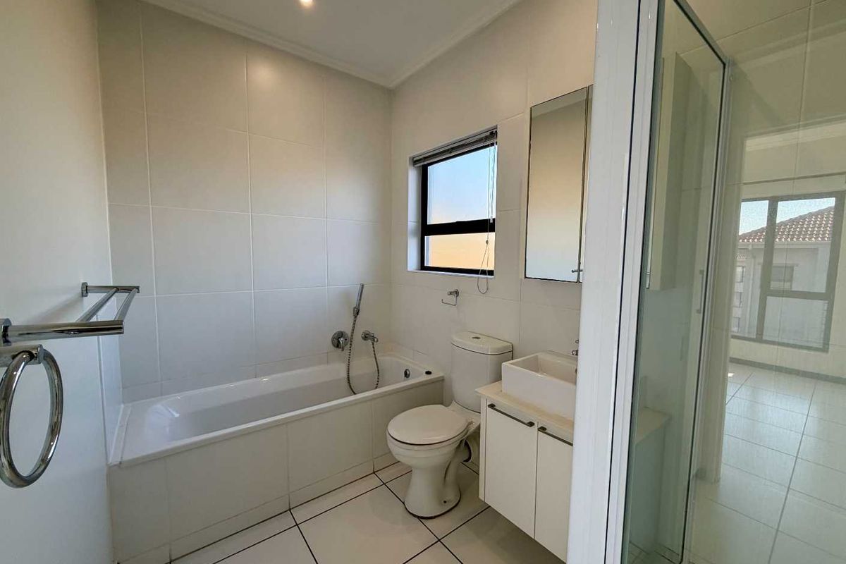 A clean, modern bathroom featuring a bathtub, separate shower enclosure, vanity with basin, and neutral wall and floor tiling.