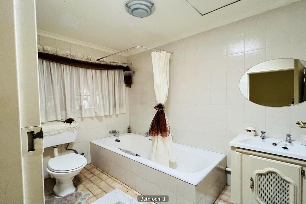 A functional bathroom featuring a built-in bathtub with shower attachment, a pedestal vanity, and a standard toilet, finished with neutral wall tiles.