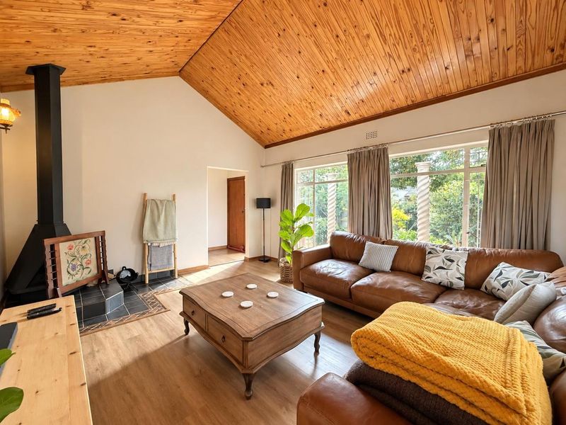 Spacious living room featuring a vaulted timber ceiling, a prominent freestanding fireplace with a tiled hearth, and large windows overlooking the garden.