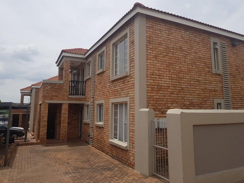 A two-story apartment building featuring a face brick facade, tiled roof, paved driveway, and a secure gated entrance.