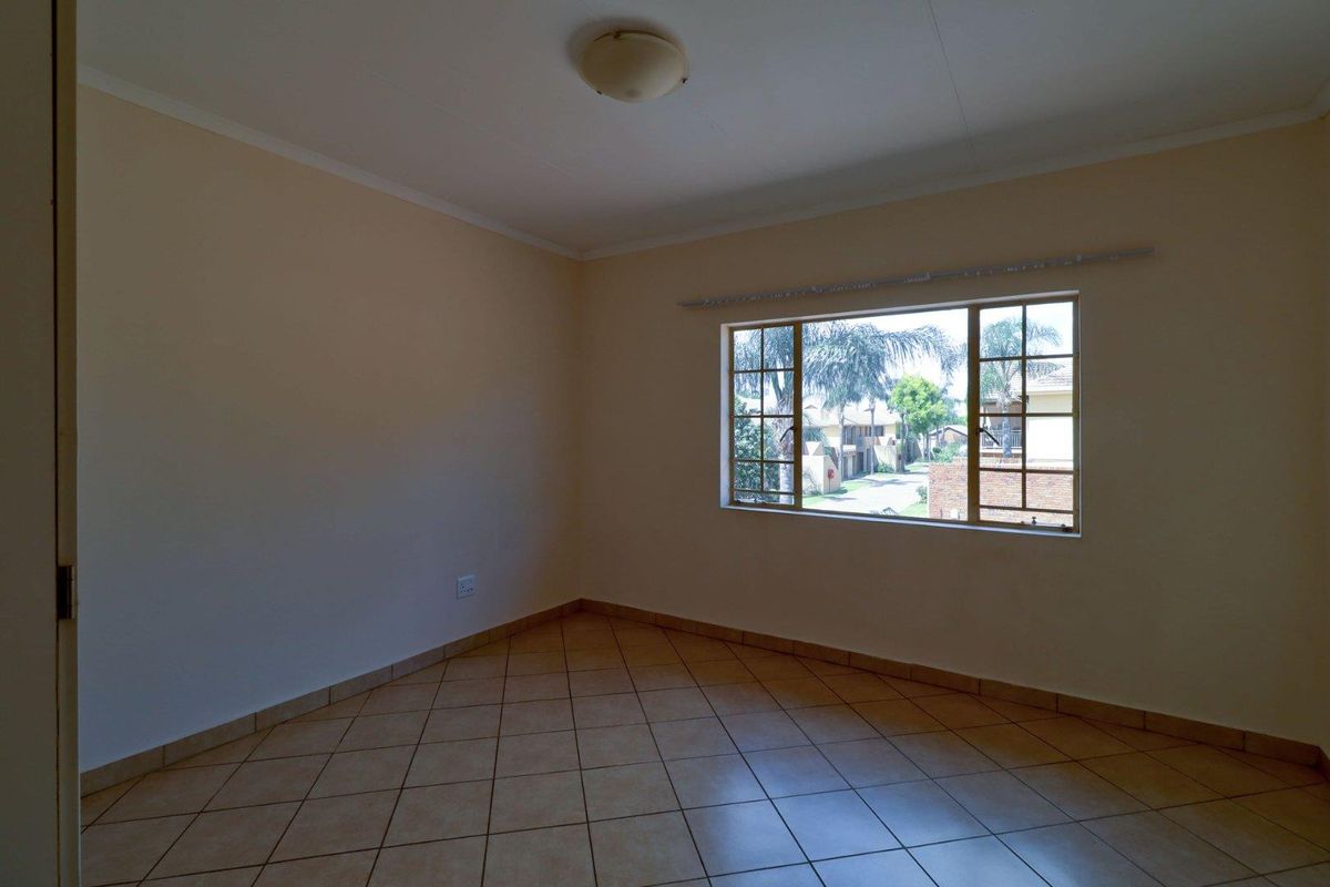 An empty bedroom featuring neutral walls, tiled flooring, and a window with security bars, offering a blank canvas for personalization.