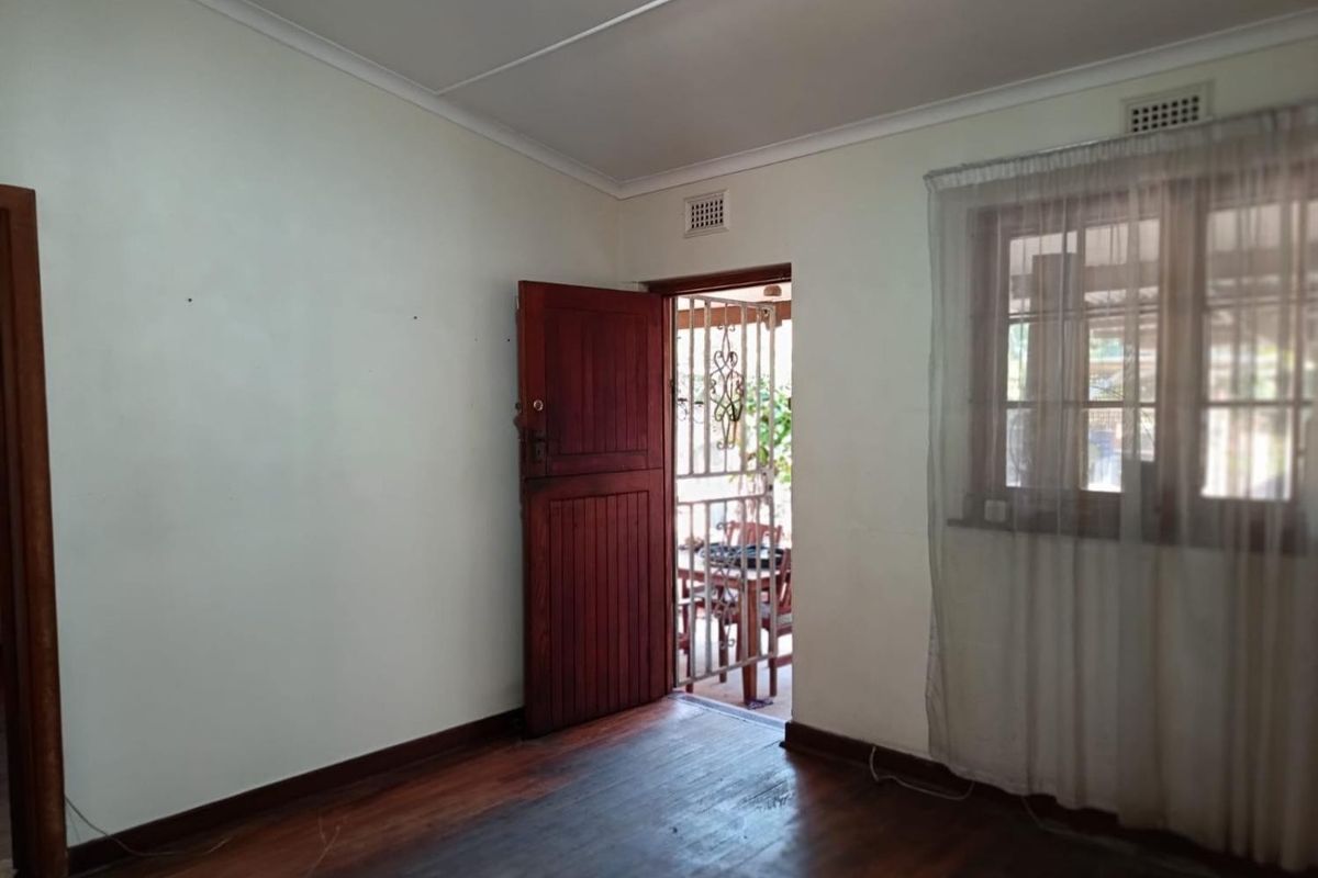 An empty bedroom featuring original timber flooring, a timber door leading to an outdoor area, and a security gate.
