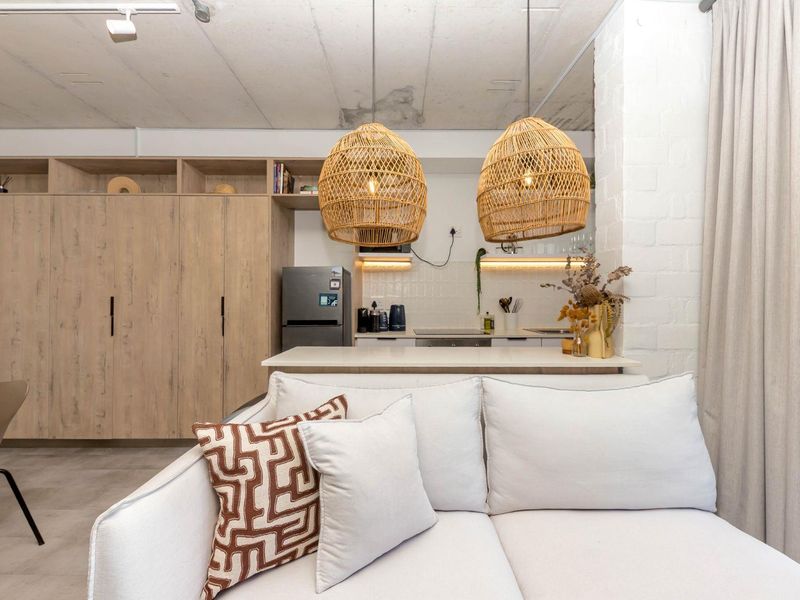 Modern open-plan living area featuring a compact kitchen with built-in cabinetry, stone countertops, and an industrial-style exposed concrete ceiling.