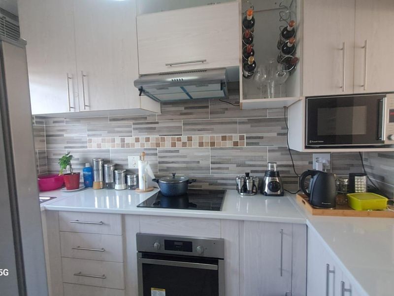 A modern, well-maintained kitchen featuring light wood-finish cabinetry, stone countertops, a tiled backsplash, and integrated appliances including an oven, hob, and microwave.