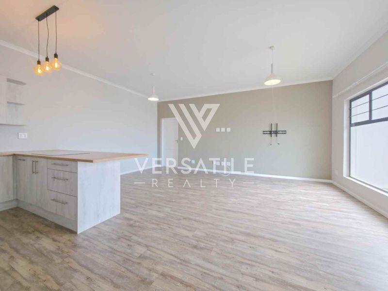 Spacious open-plan living area featuring modern laminate flooring, a kitchen island with cabinetry, and contemporary pendant lighting in a neutral color palette.