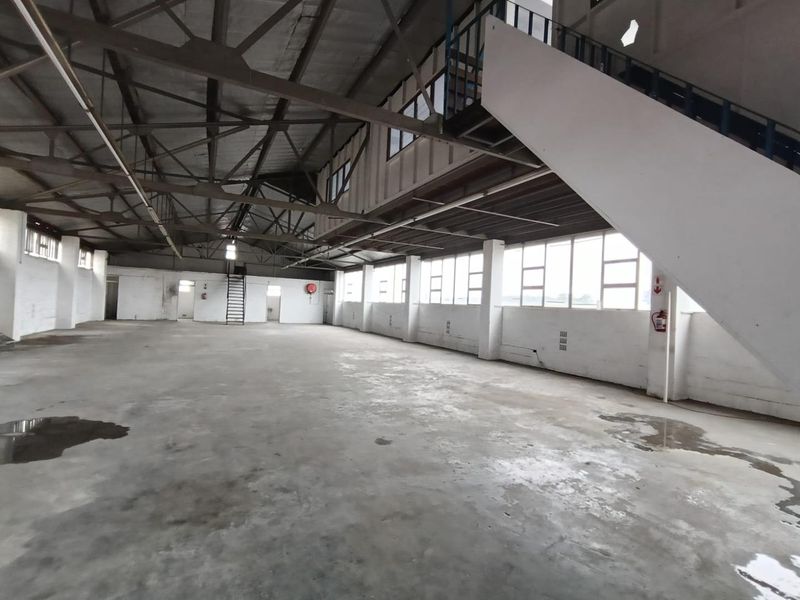 Spacious industrial warehouse area featuring exposed steel roof trusses, concrete flooring, and a metal staircase, offering a versatile open-plan layout.