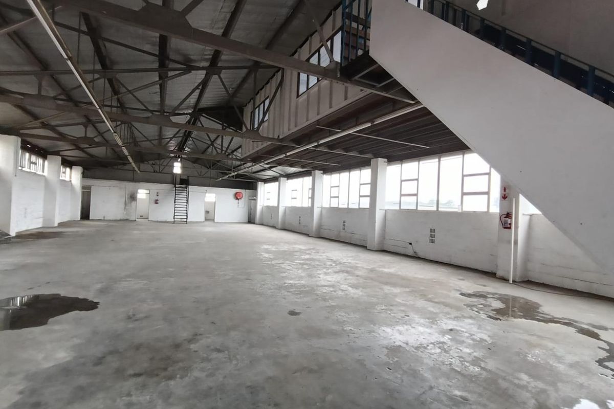 Spacious industrial warehouse area featuring exposed steel roof trusses, concrete flooring, and a metal staircase, offering a versatile open-plan layout.