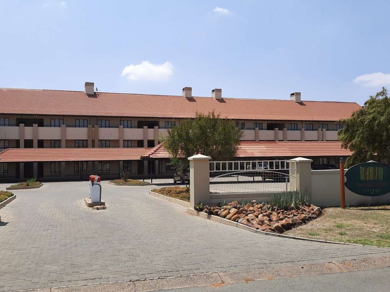 Front elevation of the Savannah Village apartment complex featuring a paved driveway, secure gated entrance, and traditional tiled roof architecture.