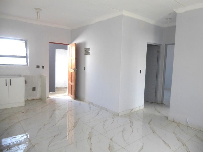 An open-plan living and kitchen area featuring marble-look floor tiles, incomplete cabinetry, and neutral walls, offering a blank canvas for interior design.