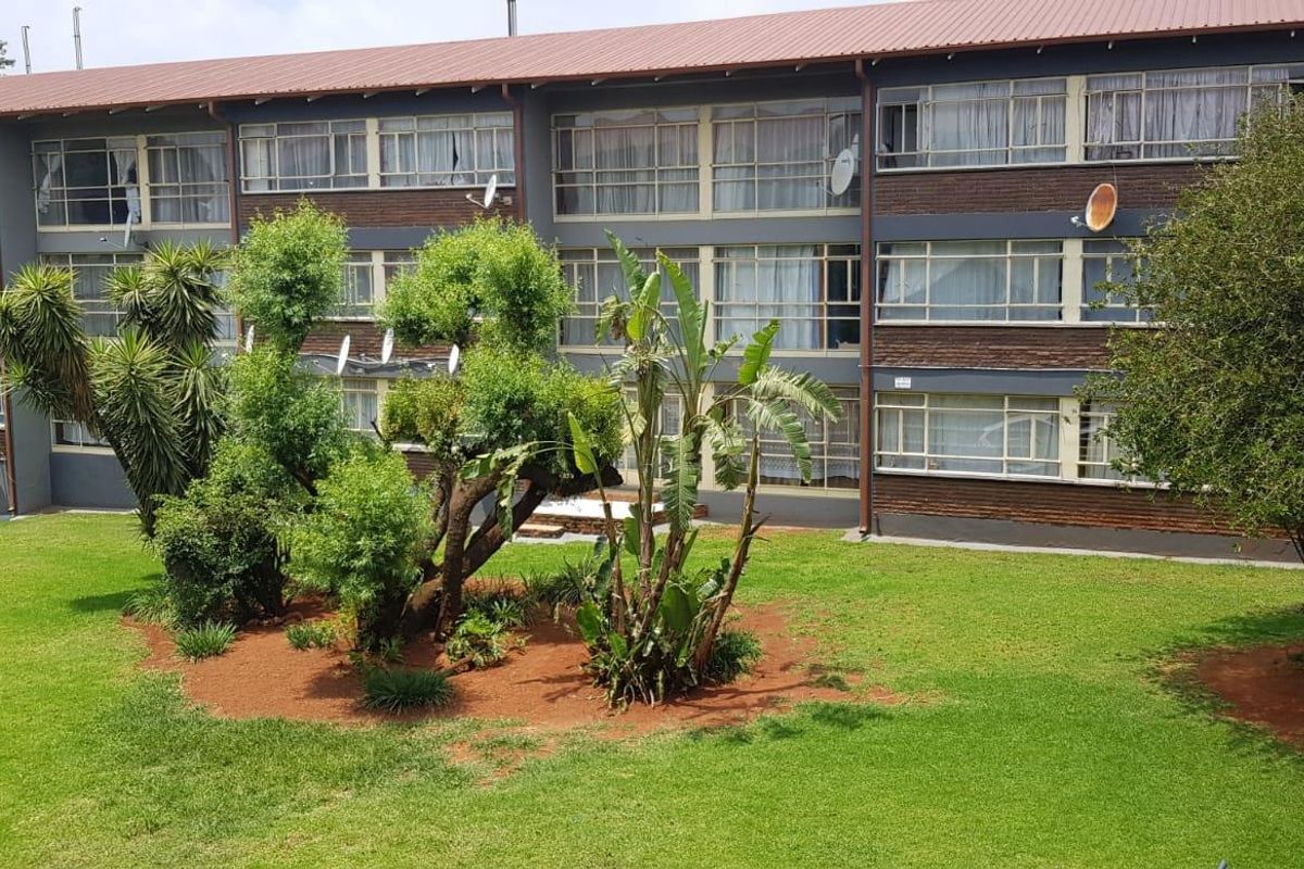 A view of the rear elevation of a multi-story apartment building featuring brick construction, large windows, and a well-maintained communal garden area.