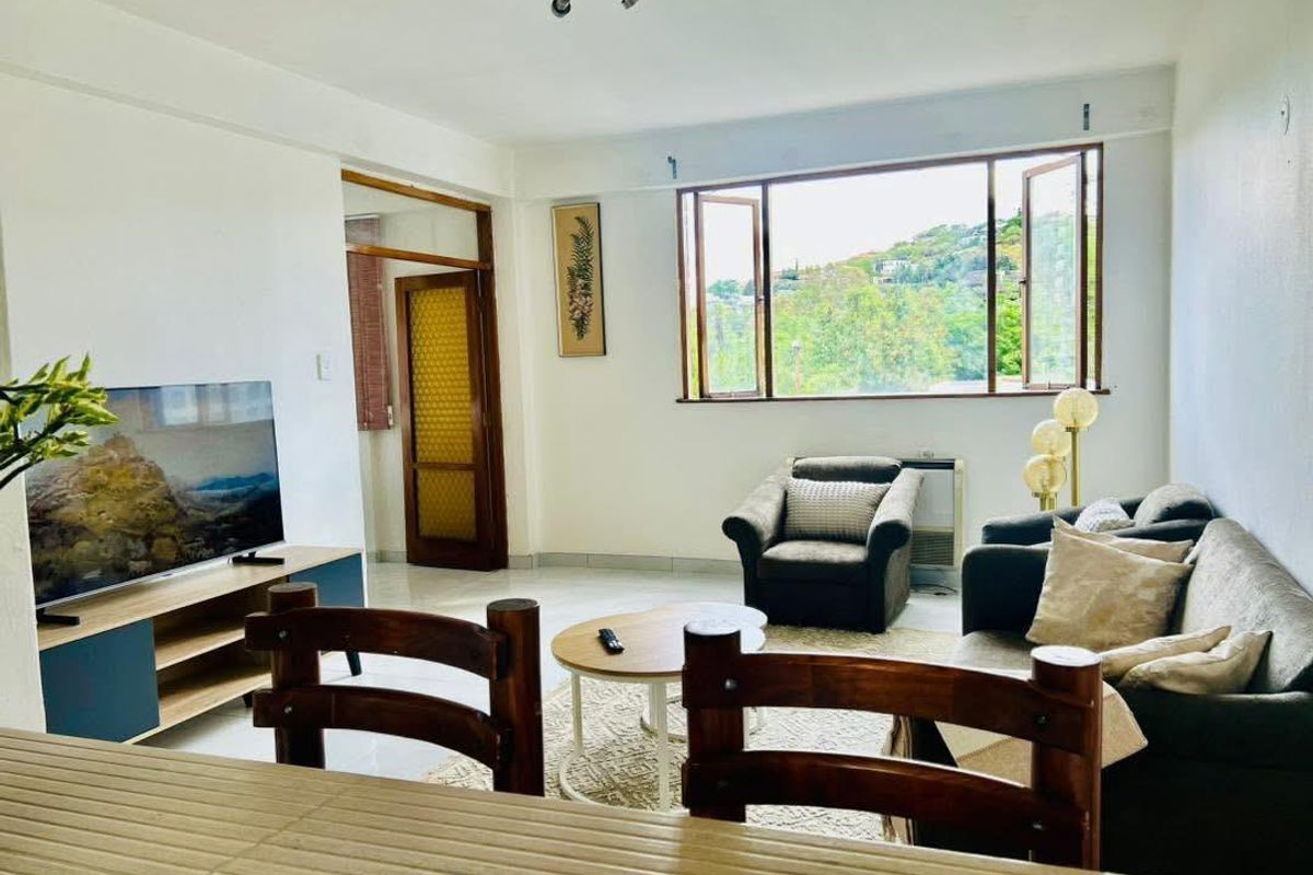 Open plan living area featuring tiled flooring and large windows that provide natural light and views of the surrounding greenery.