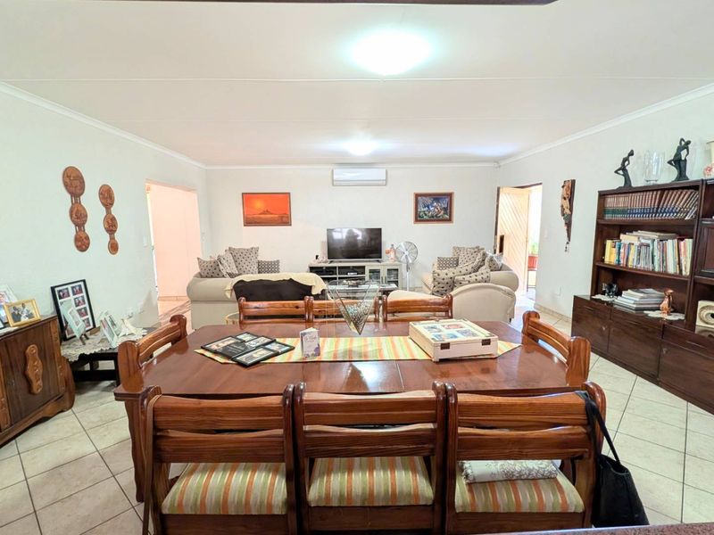 Spacious open-plan living and dining area featuring tiled flooring, coved ceilings, and a wall-mounted air conditioning unit.