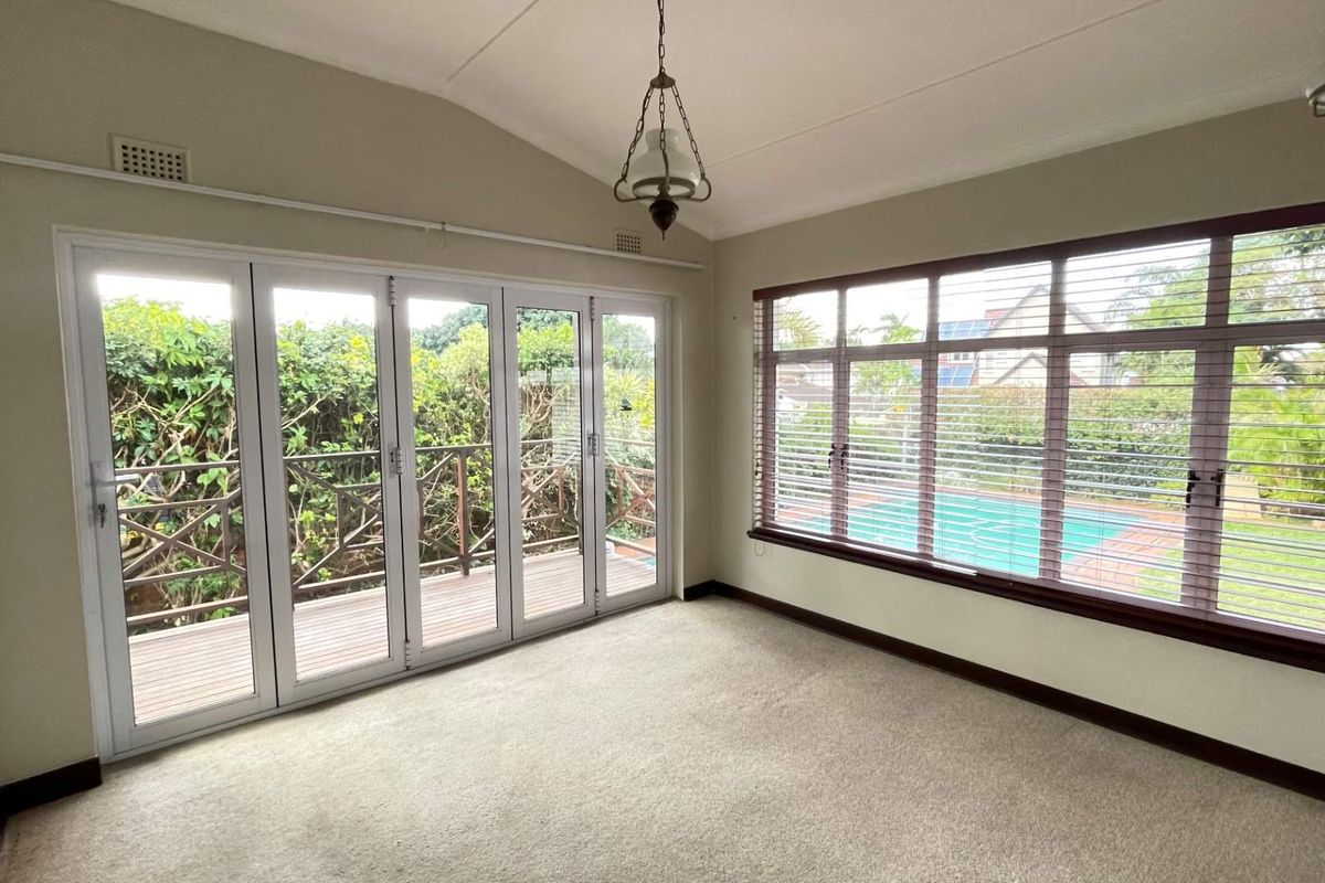 Bright and spacious living area featuring large windows, carpet flooring, and bi-fold doors opening onto an outdoor timber deck with pool views.
