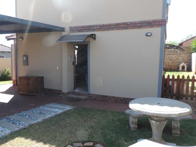 Rear exterior view of the property featuring a covered patio area, brick paving, and a small garden with a wooden picket fence.