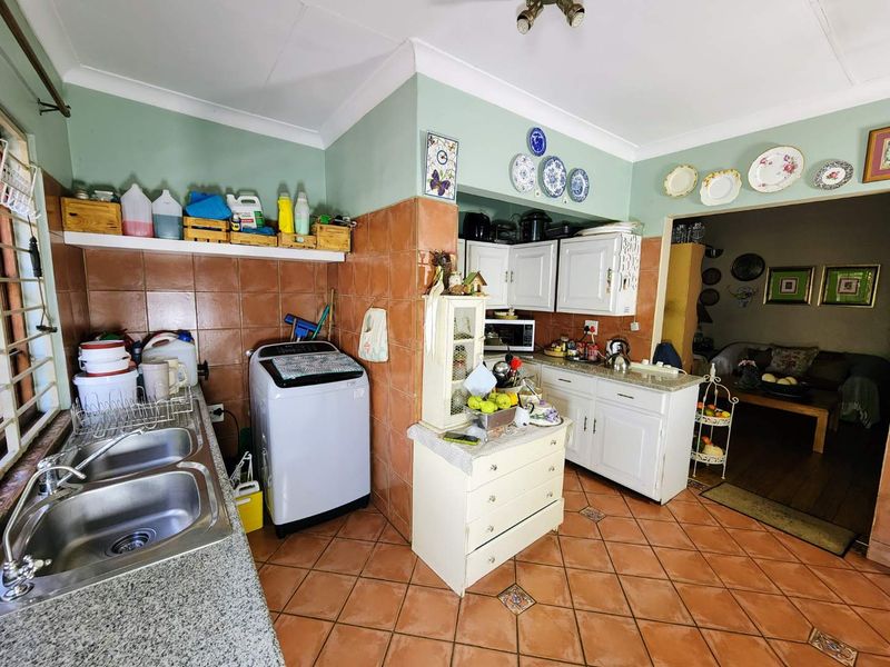 A functional kitchen featuring granite countertops, double stainless steel sink, and tiled splashbacks, with integrated cabinetry and space for laundry appliances.