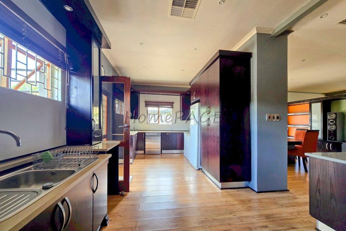A spacious kitchen featuring dark wood cabinetry, laminate flooring, and integrated appliances, flowing into an adjacent dining area.