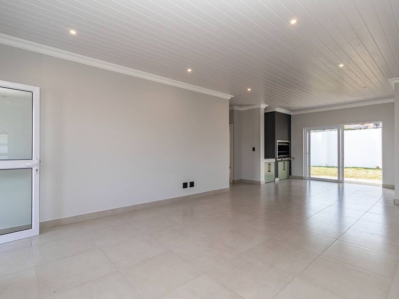 Spacious open-plan living area featuring tiled floors, recessed lighting, a built-in braai, and sliding glass doors leading to the rear garden.
