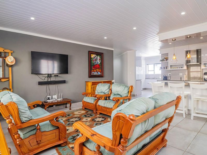 Spacious open-plan living area featuring a modern kitchen with island seating, tiled floors, and a clean tongue and groove ceiling design.