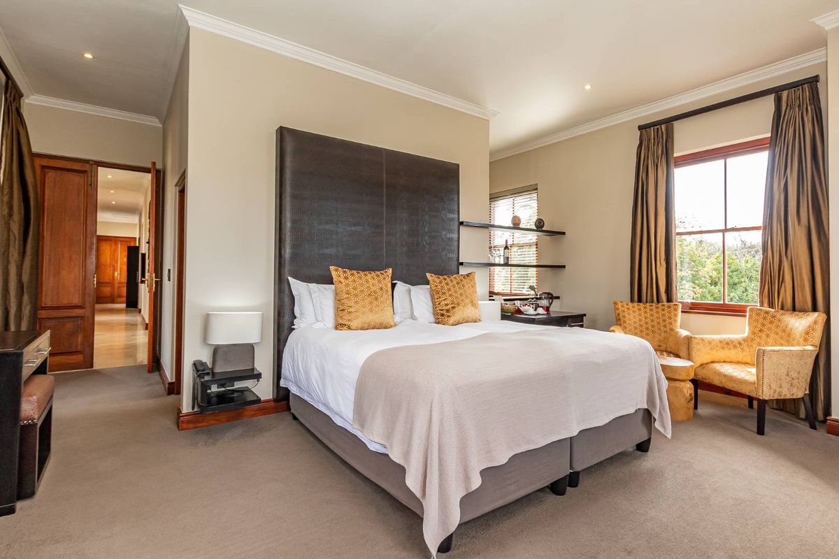 A well-appointed bedroom featuring a tall upholstered headboard, recessed ceiling lighting, crown molding, and large windows with views.
