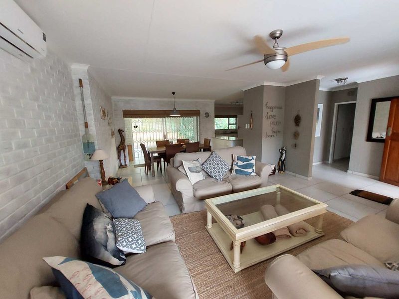 Spacious open-plan living and dining area featuring tiled floors, a brick feature wall, ceiling fan, and air conditioning, with access to the patio.