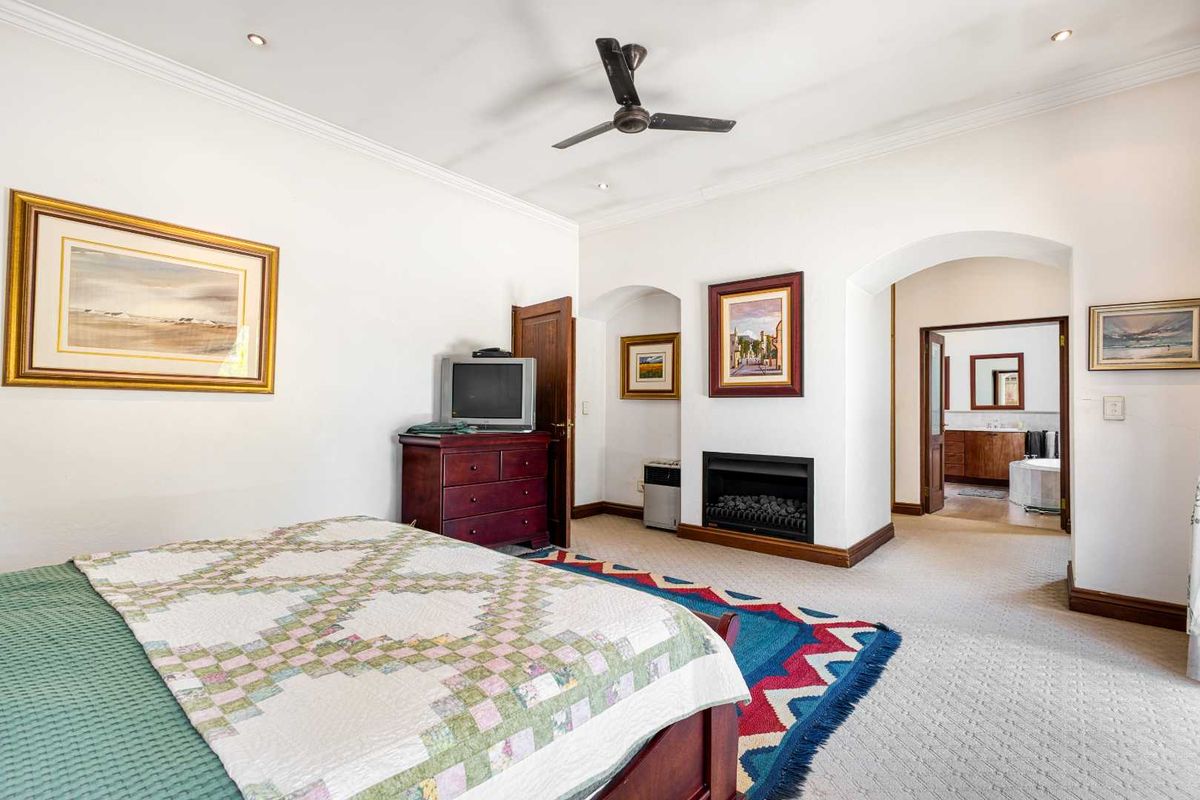 Spacious bedroom featuring a built-in fireplace, ceiling fan, and direct access to an adjoining en-suite bathroom through an arched doorway.