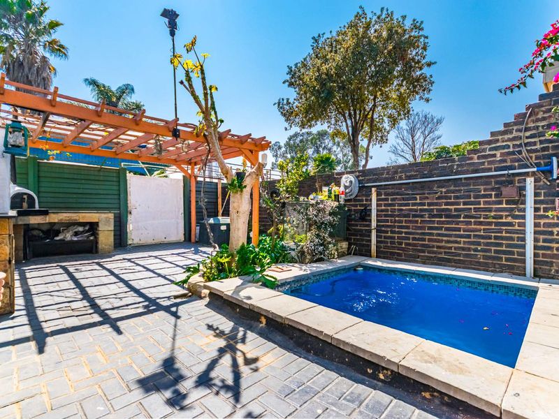 Outdoor entertainment area featuring a paved patio, built-in braai, wooden pergola, and a compact plunge pool enclosed by a brick boundary wall.