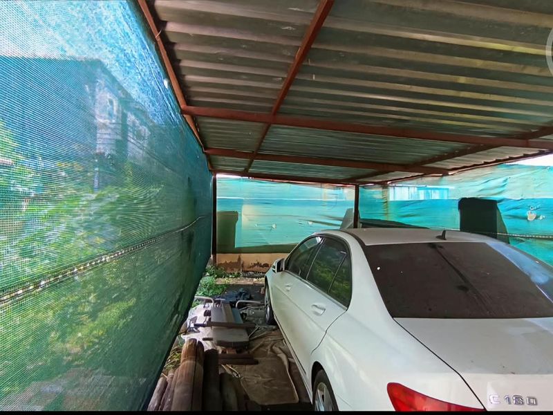 A basic covered parking area featuring a corrugated metal roof supported by a metal frame, enclosed with green shade cloth screening.