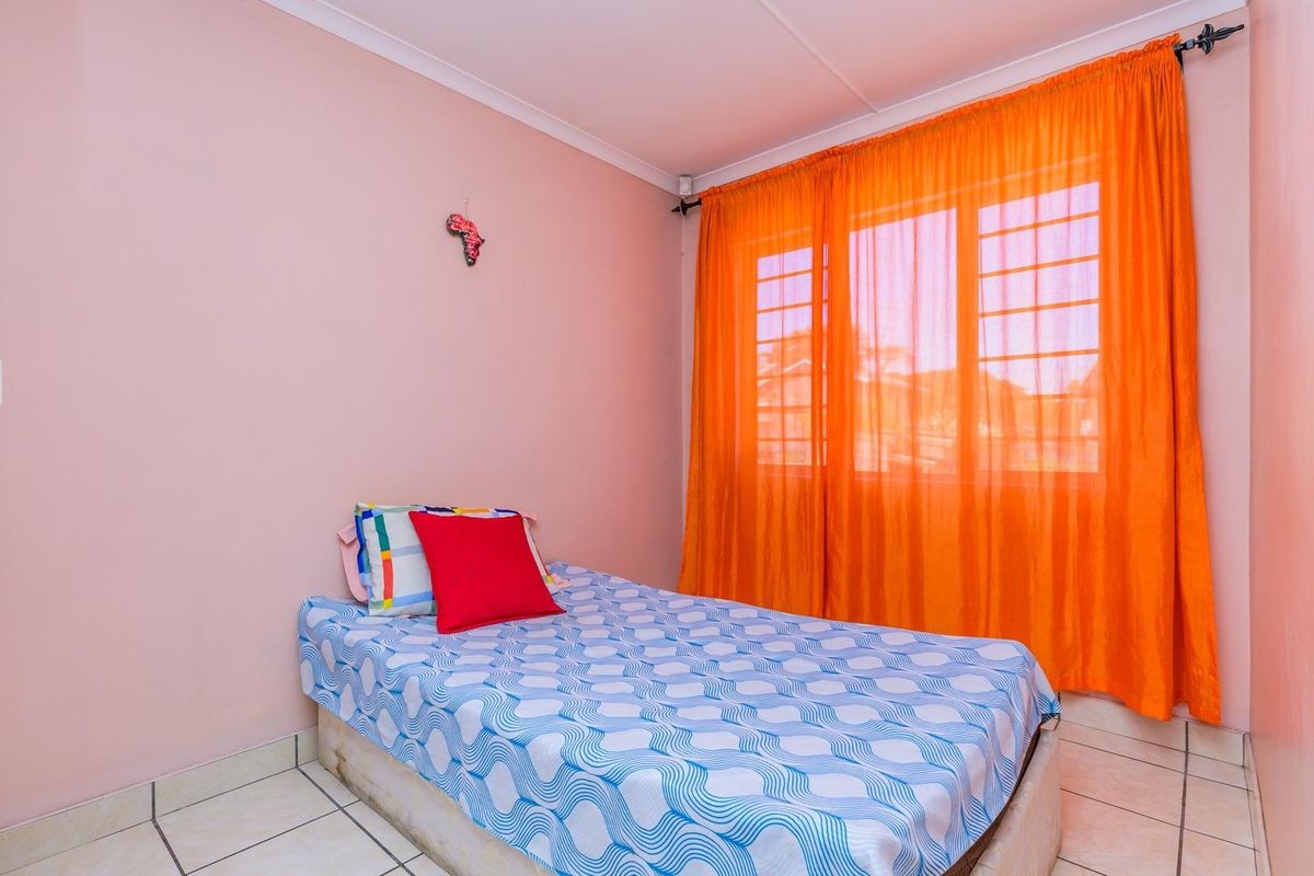 A bedroom featuring tiled flooring and a window with security bars, providing a functional space with neutral wall finishes.