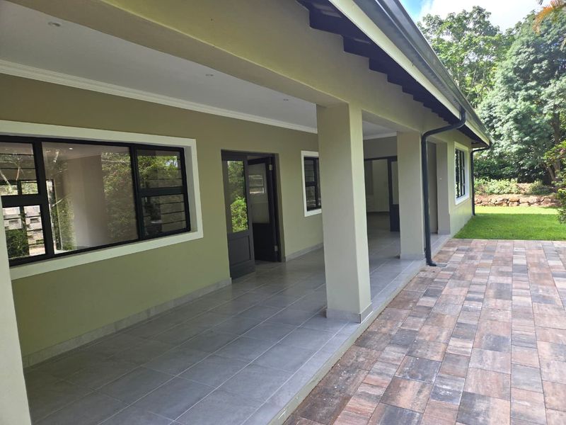 A spacious covered patio featuring tiled flooring, downlights, and aluminium window frames, providing a seamless transition to the outdoor paved area and garden.