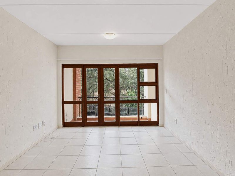 A bright, empty living area featuring neutral tiled flooring and large timber-framed glass doors leading to an outdoor balcony.