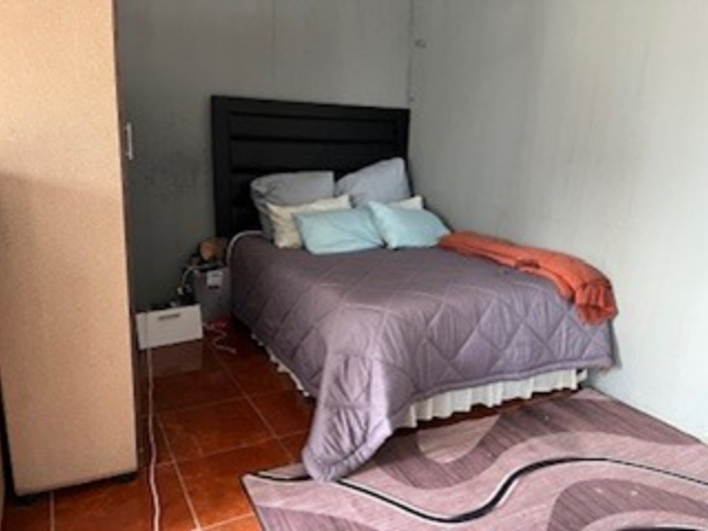 A bedroom featuring tiled flooring and plain walls, currently showing signs of wear and surface staining.