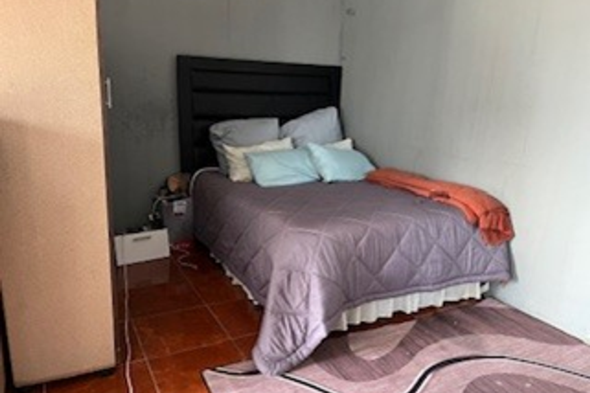 A bedroom featuring tiled flooring and plain walls, currently showing signs of wear and surface staining.