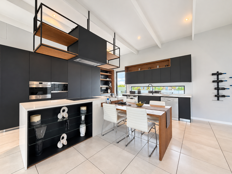 Modern, high-end kitchen featuring sleek matte black cabinetry, a central island with integrated dining, premium built-in appliances, and stylish exposed ceiling beams.