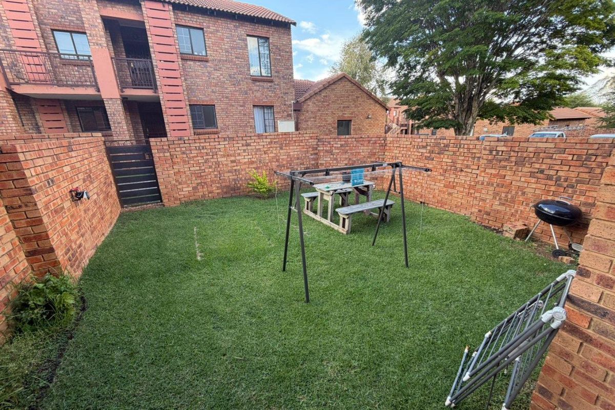A private rear garden area featuring a lawn enclosed by face-brick boundary walls, providing a secure outdoor space for the apartment unit.