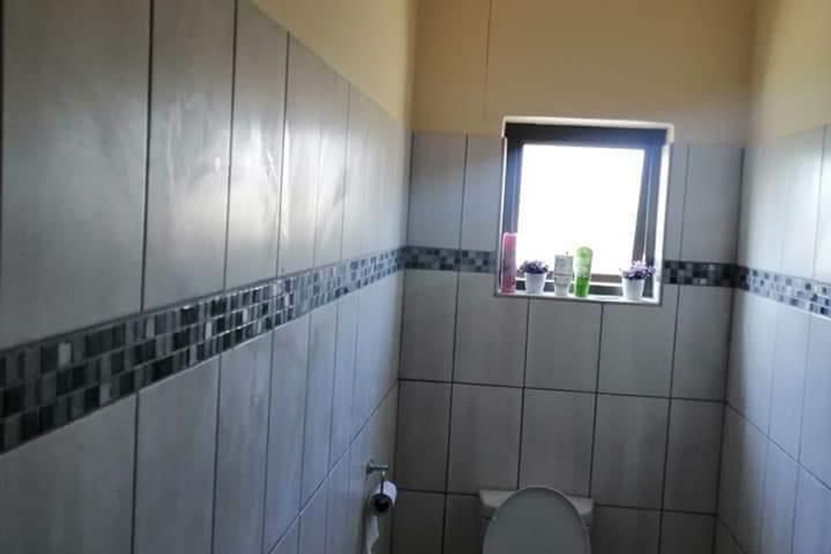 A functional bathroom featuring tiled walls with a decorative mosaic border, tiled flooring, and a window for natural light.
