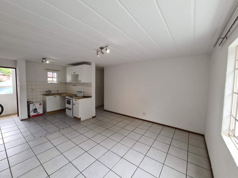 An open-plan living and kitchen area featuring tiled flooring, white cabinetry, and a functional kitchen layout in a clean, vacant space.
