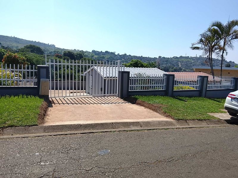 Front view of the property featuring a metal security gate, concrete driveway, and perimeter walling with views of the surrounding neighborhood.