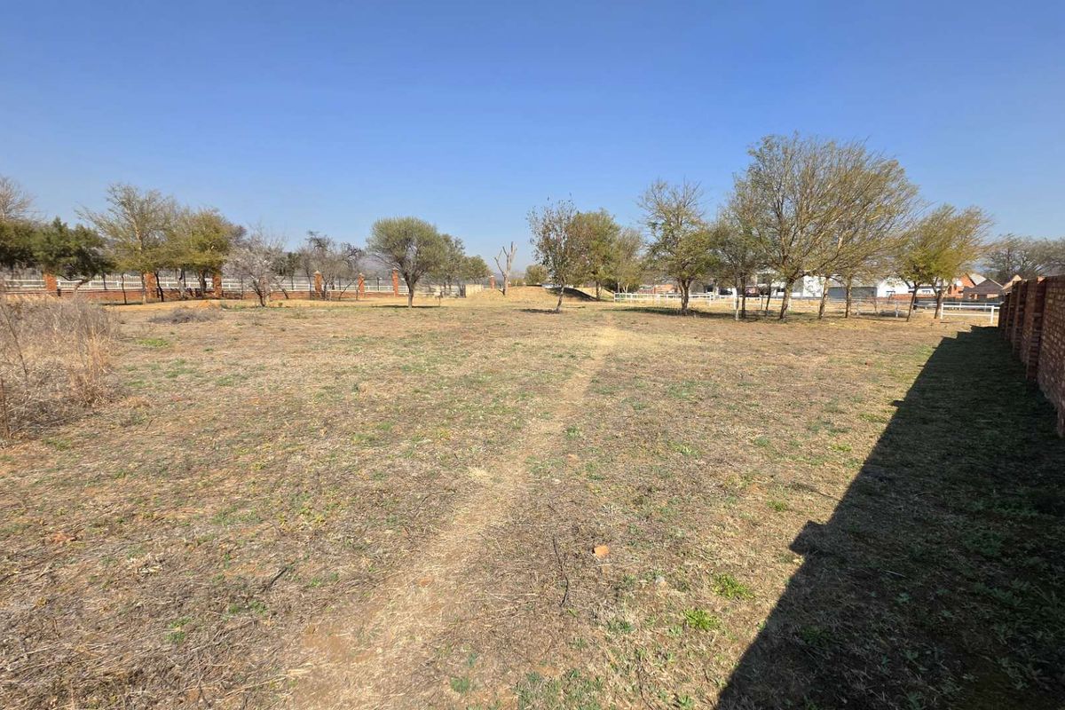 A spacious, level vacant residential plot featuring established trees and enclosed by brick boundary walls and perimeter fencing.